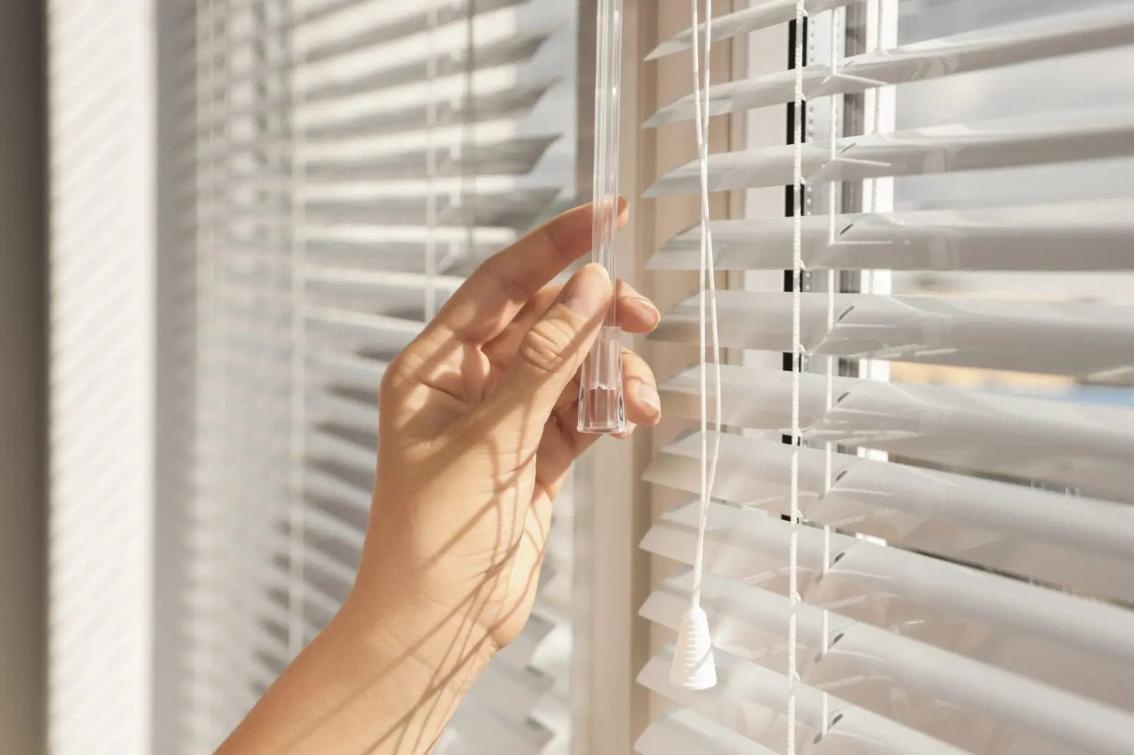A person is looking out of the window through blinds.